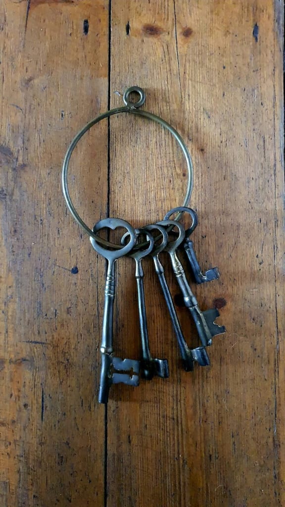 Five antique keys hang on a brass ring placed on a wooden surface.
