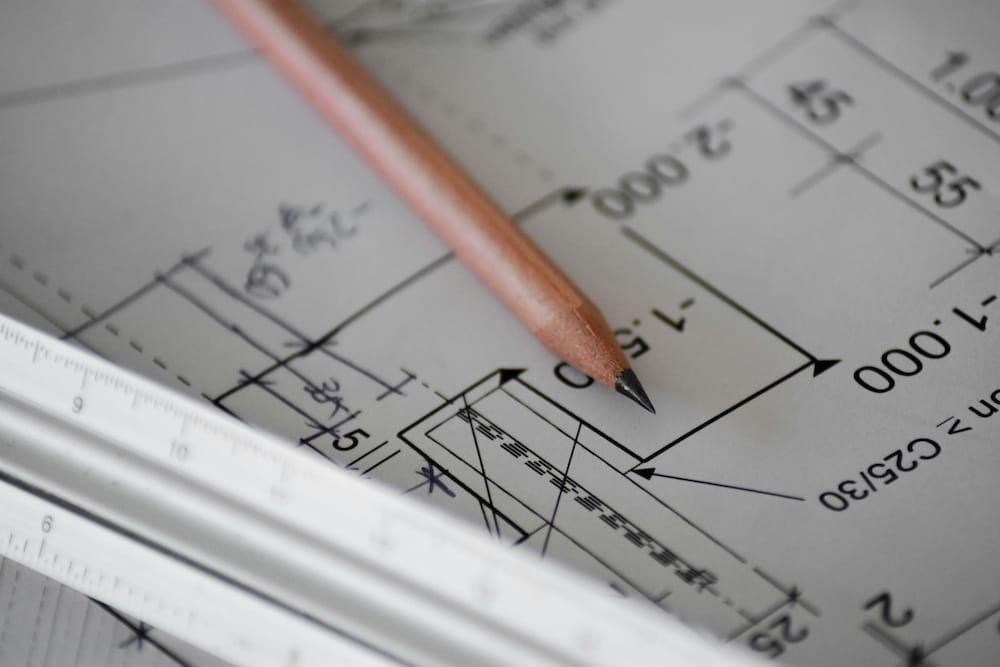 Close-up of a technical drawing with a pencil and a ruler placed on top, showing architectural measurements and details.